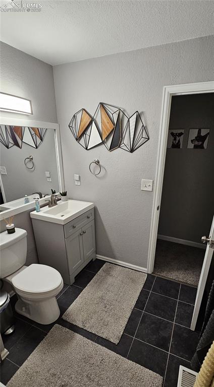 Image 16 of 40: Full bath with a textured wall, vanity and dark tile patterned flooring