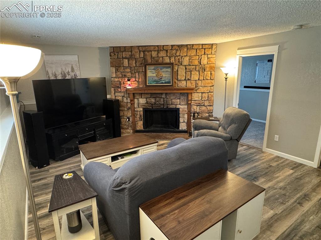 Image 19 of 40: Living room with a stone fireplace, a textured ceiling, and dark wood finis