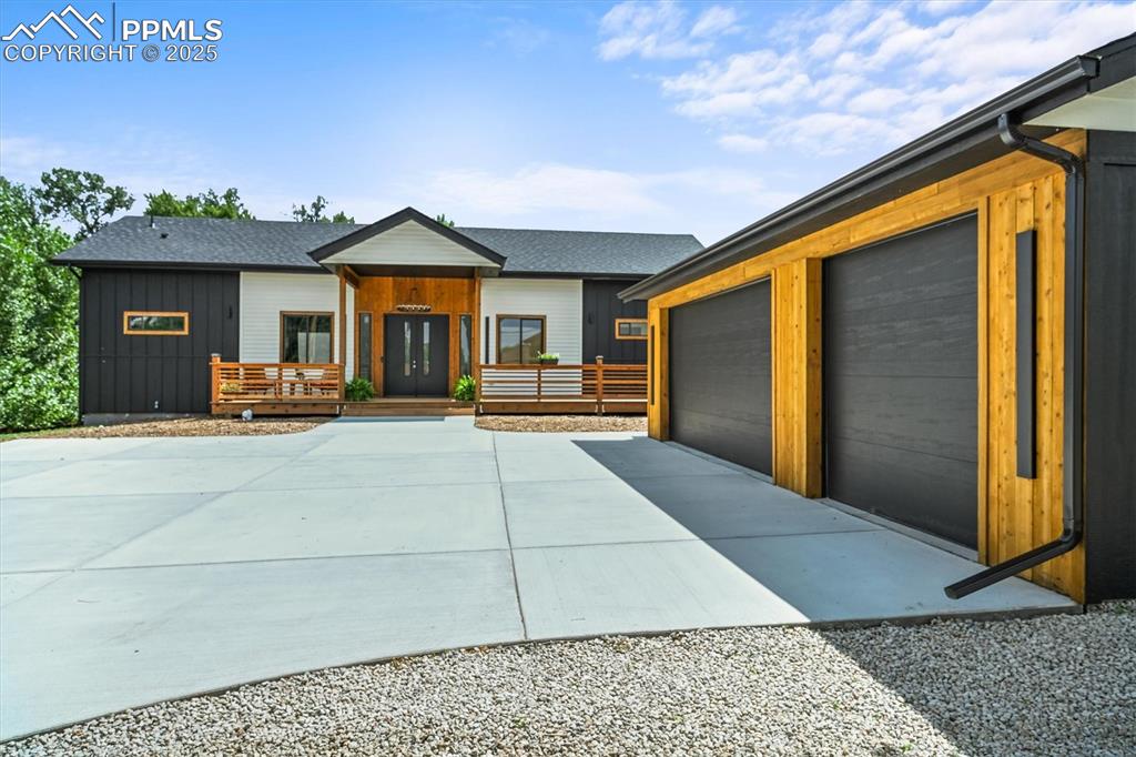 Caption: View of front of house featuring a garage, a deck, driveway, an outdoor structure, and board and bat