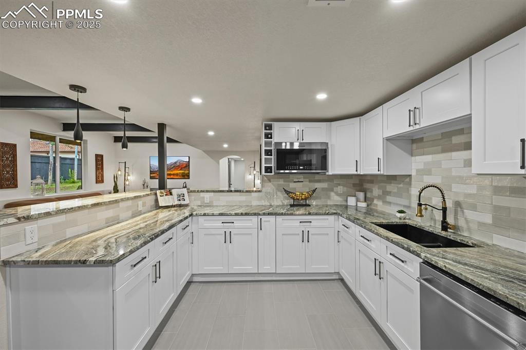 Image 24 of 47: Kitchen featuring a peninsula, light stone counters, decorative light fixtu