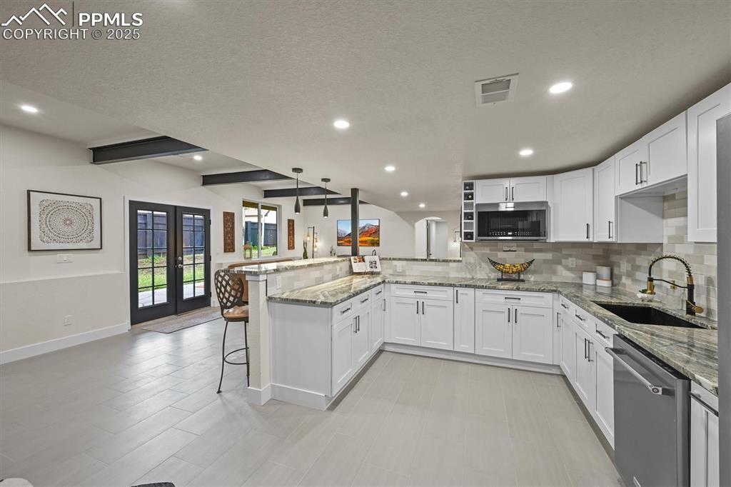 Image 25 of 47: Kitchen with a peninsula, tasteful backsplash, white cabinetry, french door