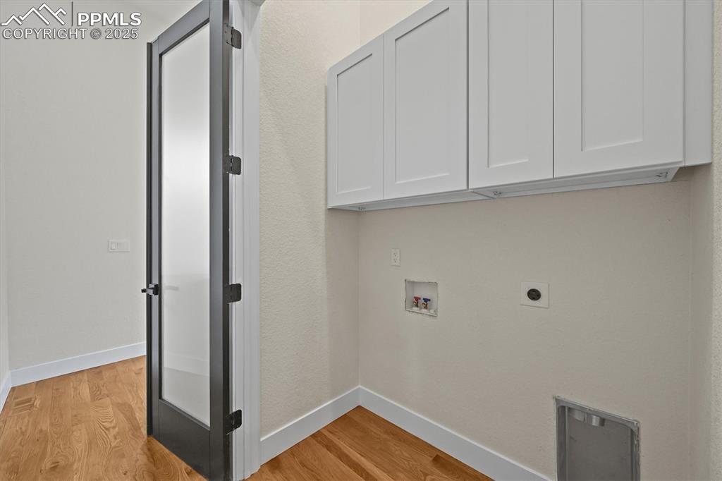 Image 29 of 47: Laundry area featuring light wood finished floors, washer hookup, cabinet s