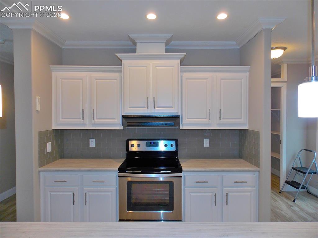 Image 7 of 33: Kitchen with stainless steel electric stove, white cabinets, crown molding,