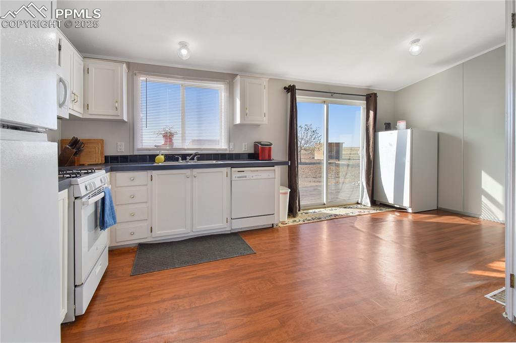 Image 14 of 34: Kitchen featuring dark countertops, white appliances, light wood finished f