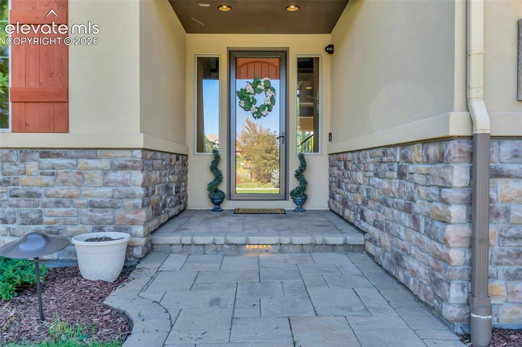 Image 18 of 50: Covered entryway featuring a stone veneer facade, paved walkway, glass-pane