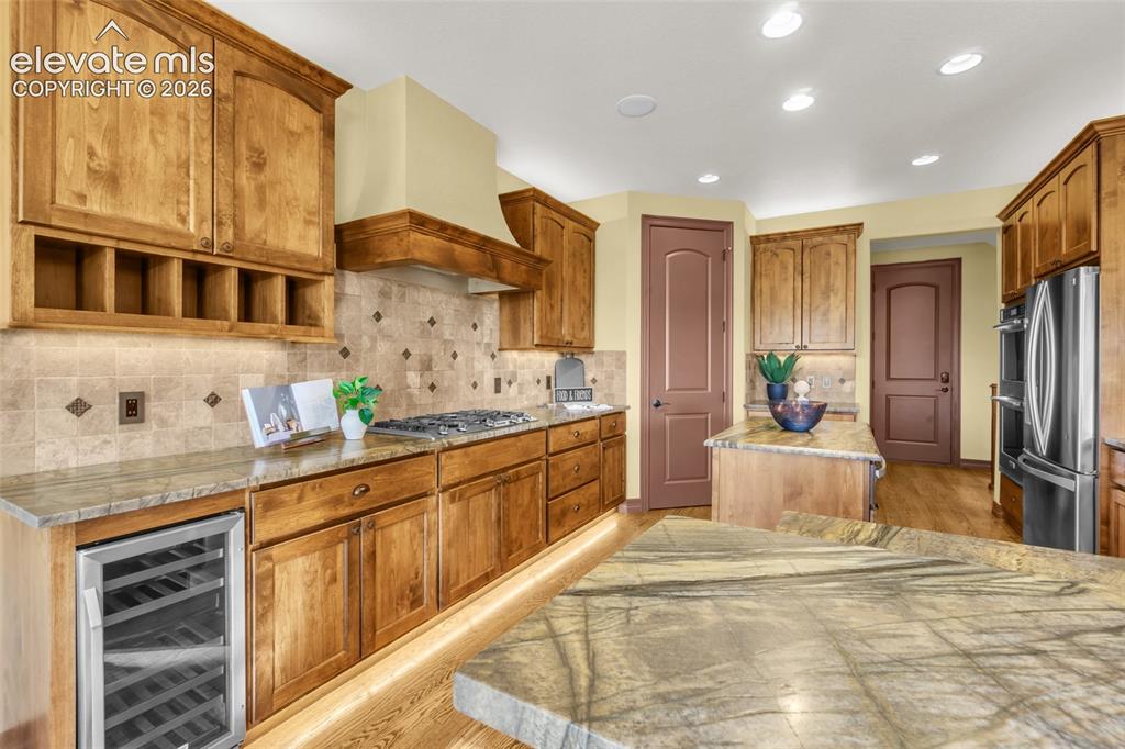 Image 27 of 50: Kitchen featuring custom wood cabinetry, natural stone countertops, a tiled
