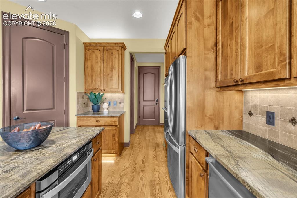 Image 28 of 50: Kitchen featuring wood cabinetry, natural stone countertops, square-tile ba