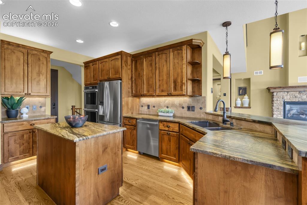 Image 30 of 50: Kitchen featuring medium-tone wood cabinetry, stone countertops, stainless 
