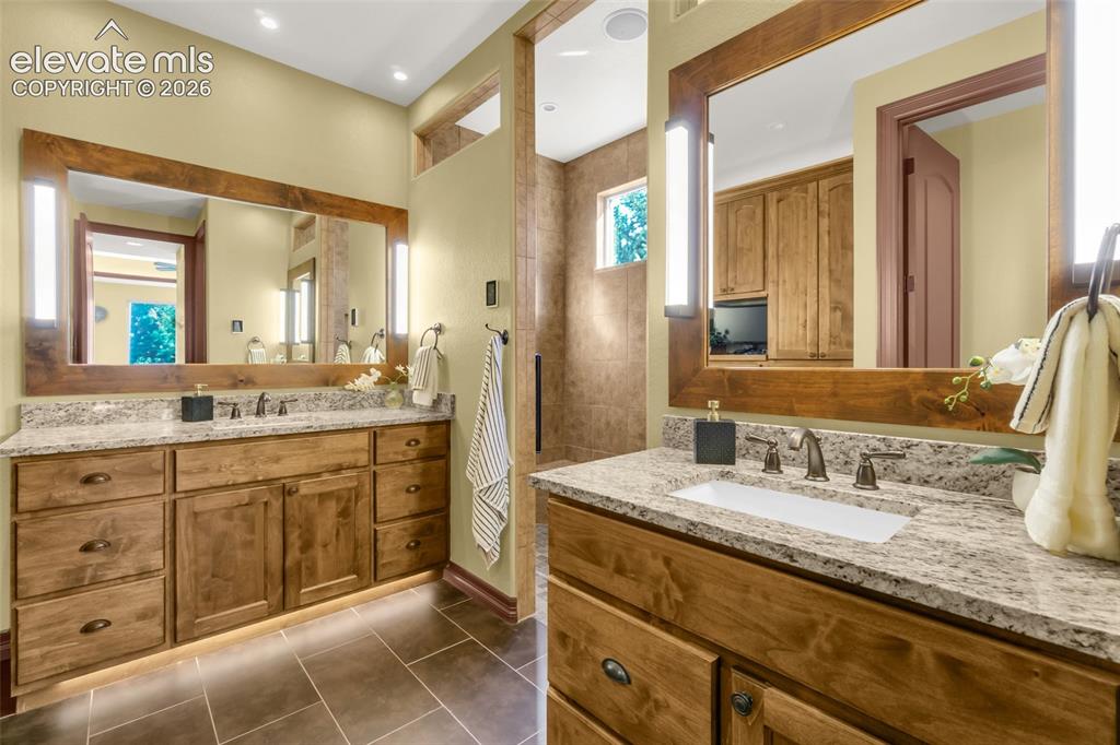 Image 35 of 50: Dual-vanity bathroom featuring custom wood cabinetry, stone countertops wit