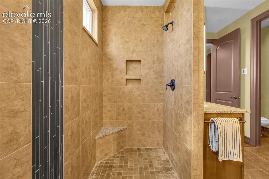 Image 37 of 50: Walk-in shower featuring oversized earth-tone wall tile, vertical dark mosa
