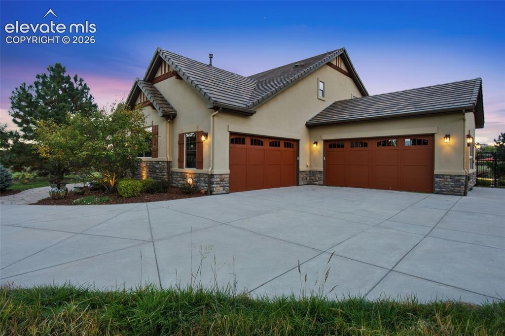 Image 4 of 50: Stucco exterior featuring stone veneer accents, concrete driveway, three-ca