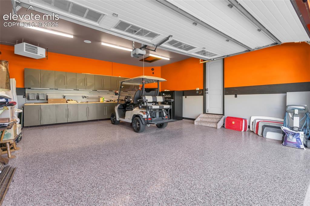 Image 47 of 50: Finished garage featuring epoxy flooring, extensive wall-mounted cabinetry,