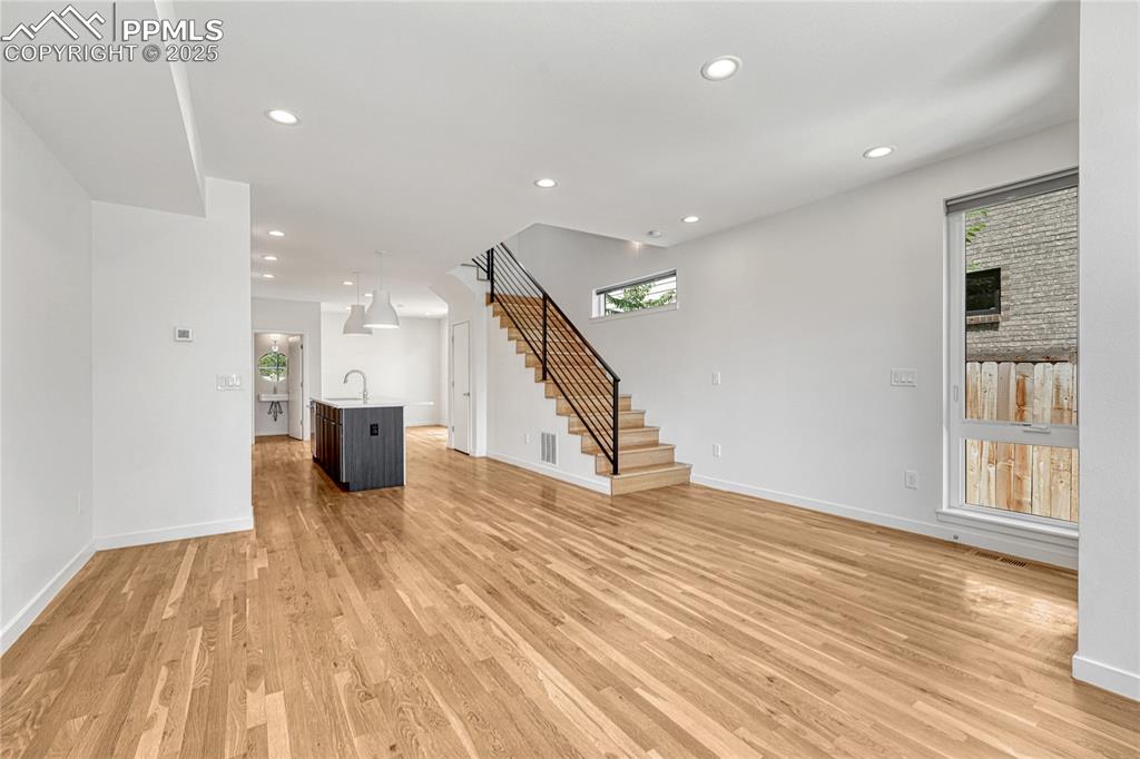 Image 6 of 49: Unfurnished living room featuring stairs, light wood finished floors, and r