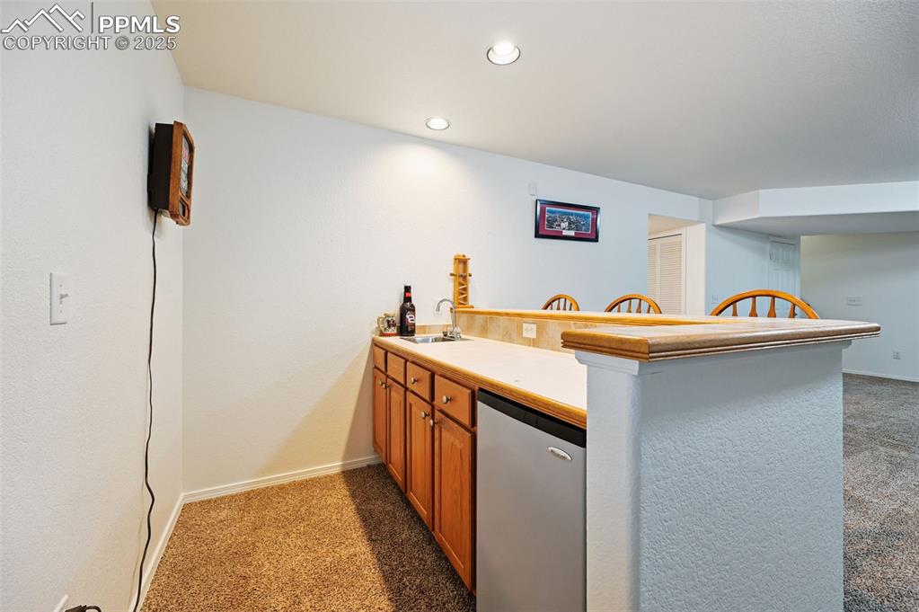 Image 27 of 45: Kitchen featuring light colored carpet, a peninsula, brown cabinets, recess