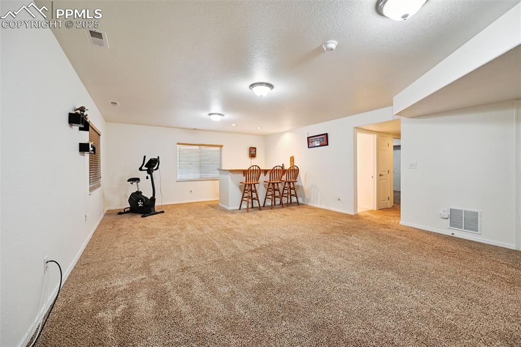 Image 31 of 45: Exercise room featuring a textured ceiling, carpet flooring, and a dry bar