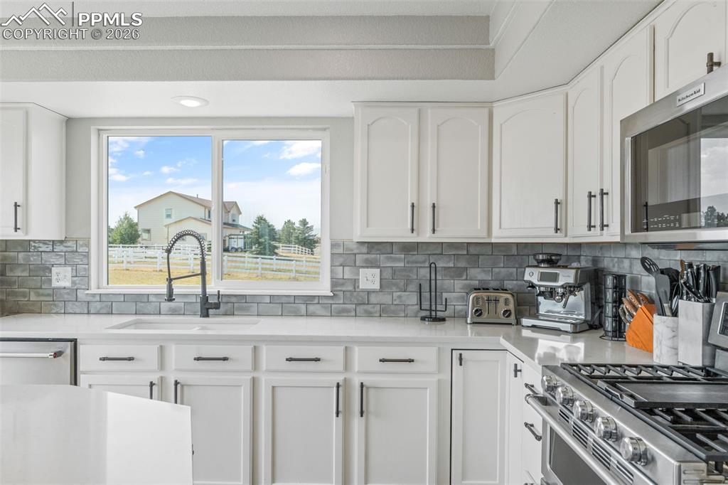 Image 15 of 47: Kitchen featuring stainless steel appliances, light stone counters, white c
