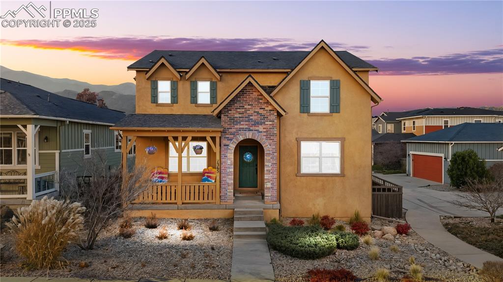 Caption: Traditional-style home featuring stucco siding, covered porch, a garage, and a shingled roof