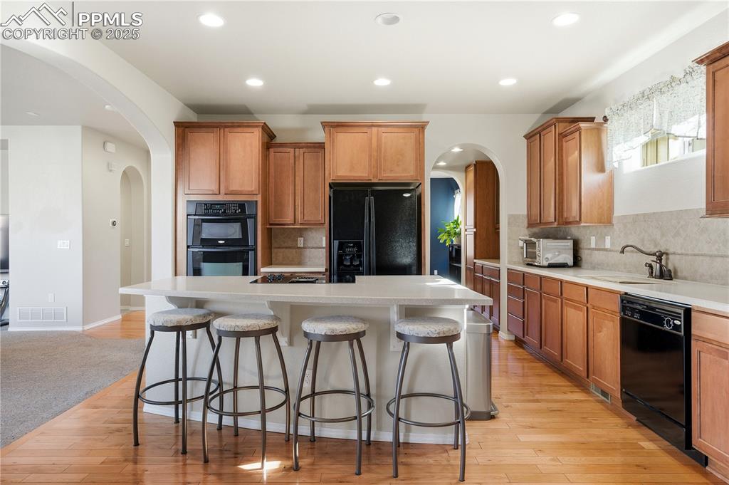 Image 10 of 42: Kitchen with arched walkways, brown cabinets, a kitchen bar, and recessed l