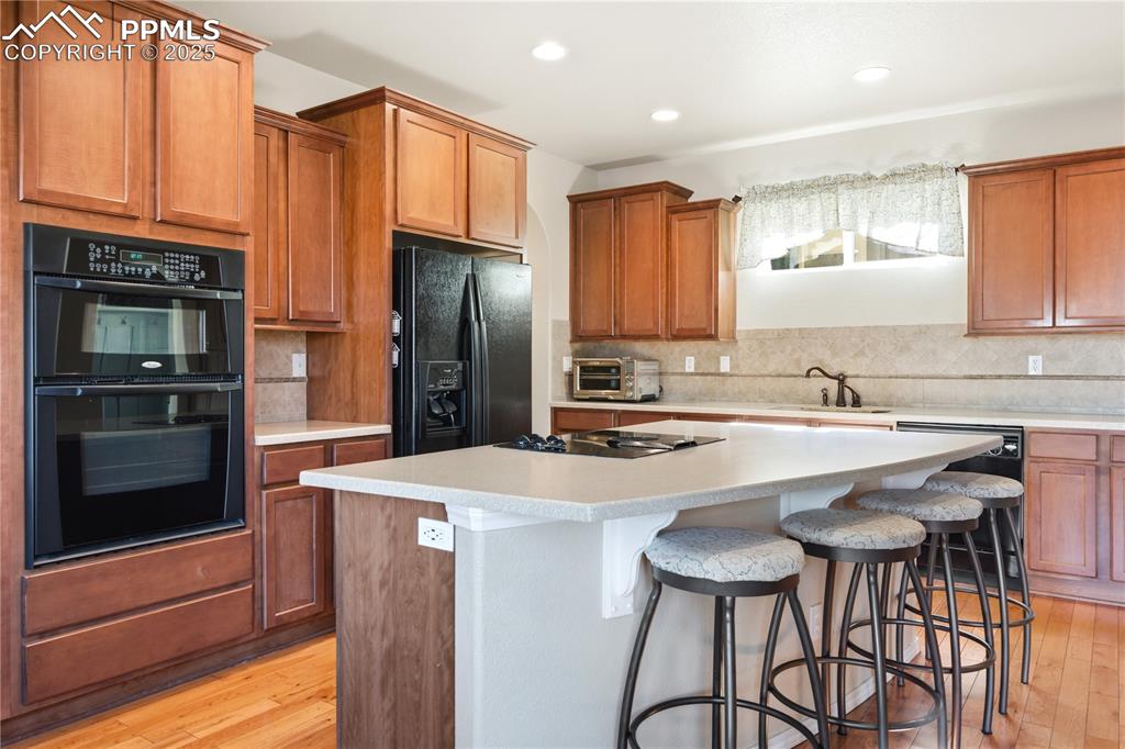 Image 11 of 42: Kitchen with brown cabinets, black appliances, light wood-type flooring, de