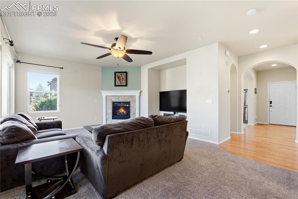 Image 15 of 42: Living area featuring light colored carpet, a tiled fireplace, arched walkw