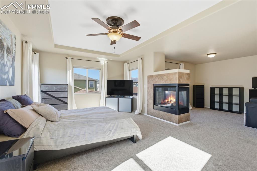 Image 18 of 42: Carpeted bedroom featuring a multi sided fireplace, a ceiling fan, and a tr