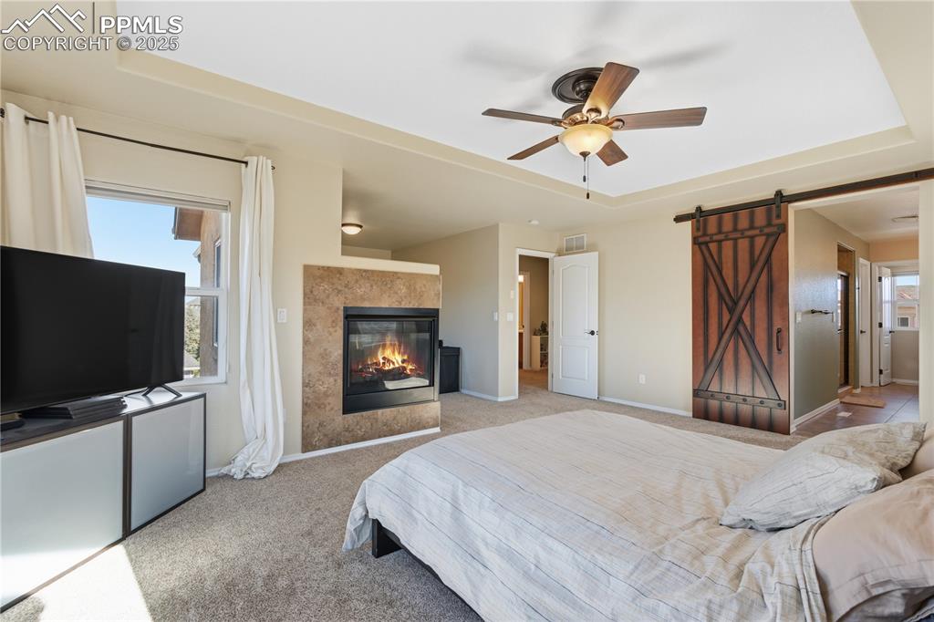 Image 19 of 42: Carpeted bedroom featuring a barn door, a raised ceiling, a ceiling fan, an