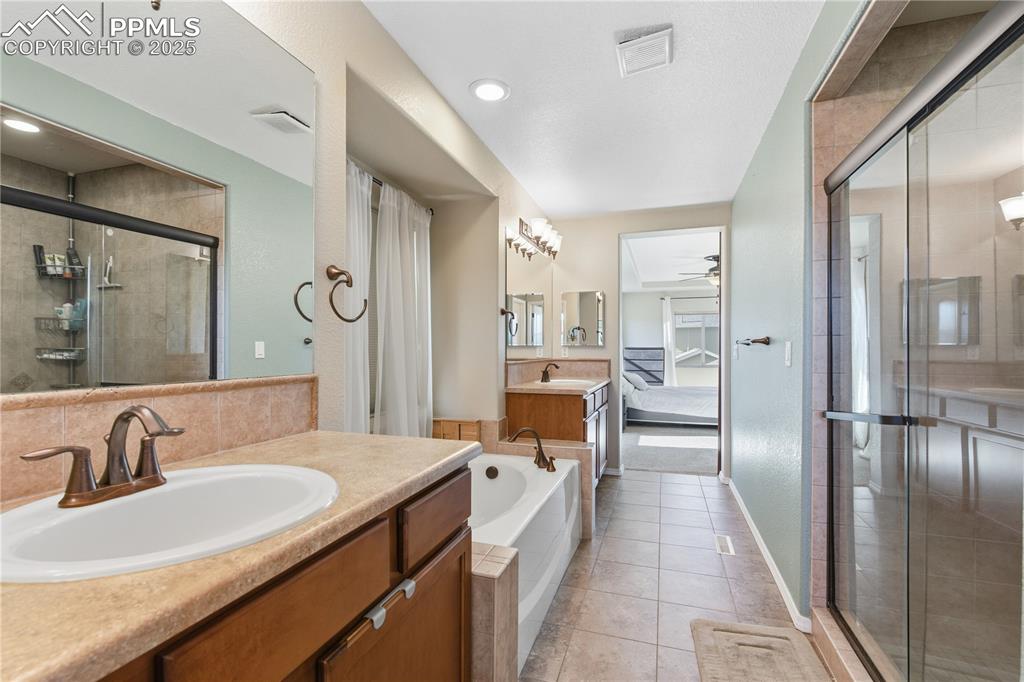 Image 23 of 42: Ensuite bathroom featuring two vanities, a shower stall, light tile pattern