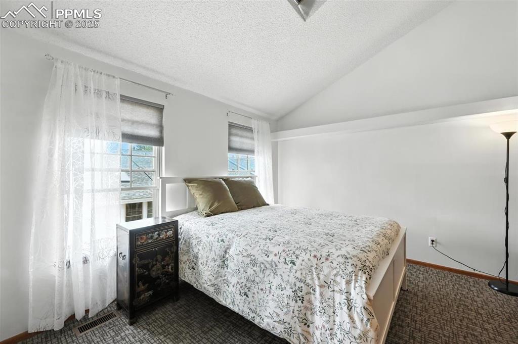 Image 14 of 25: Bedroom featuring dark colored carpet, lofted ceiling, and a textured ceili