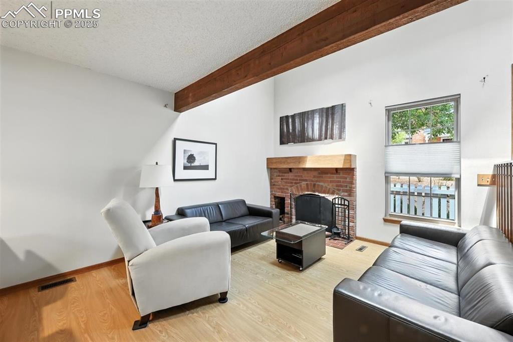 Image 5 of 25: Living area with a textured ceiling, a fireplace, light wood-type flooring,