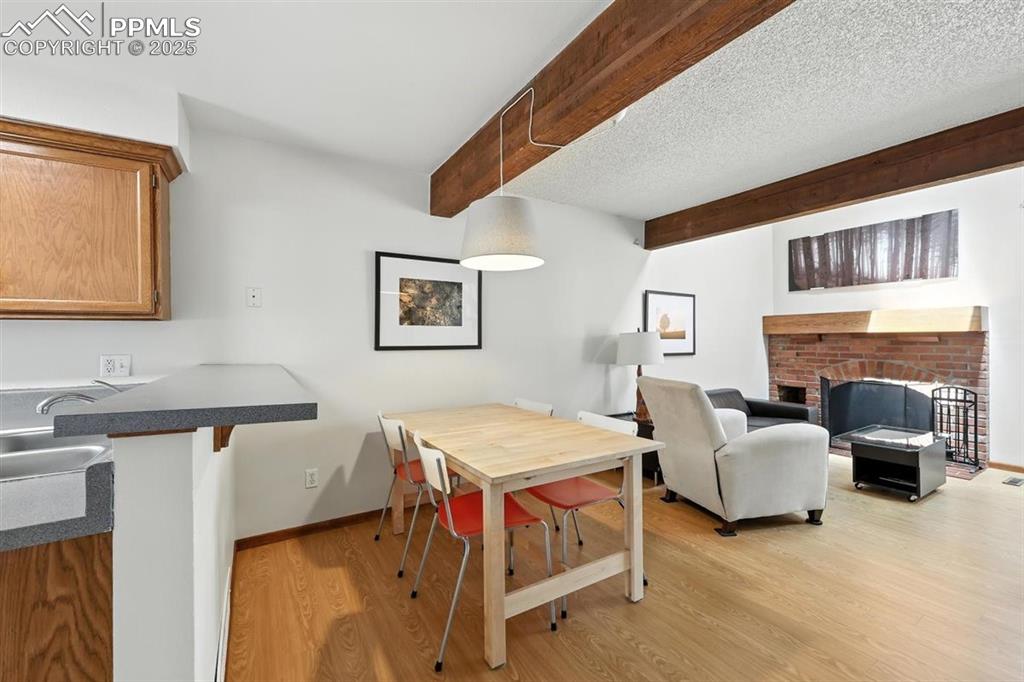Image 8 of 25: Dining area featuring light wood-style floors, beamed ceiling, and a firepl
