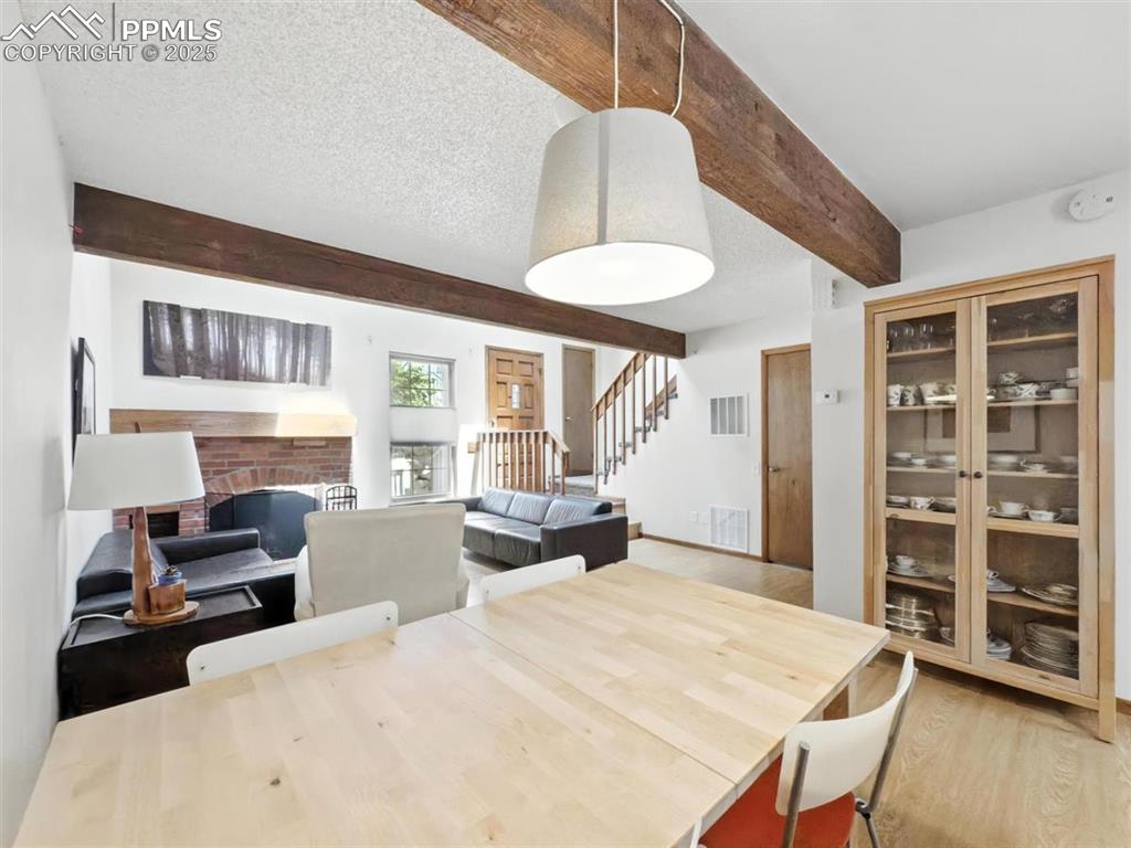 Image 9 of 25: Dining area with light wood finished floors, beamed ceiling, stairway, a fi