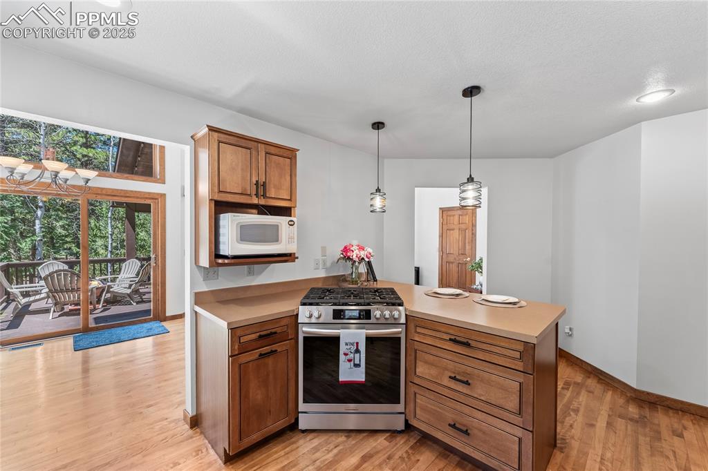 Image 10 of 49: Kitchen with stainless steel gas range oven, white microwave, light counter
