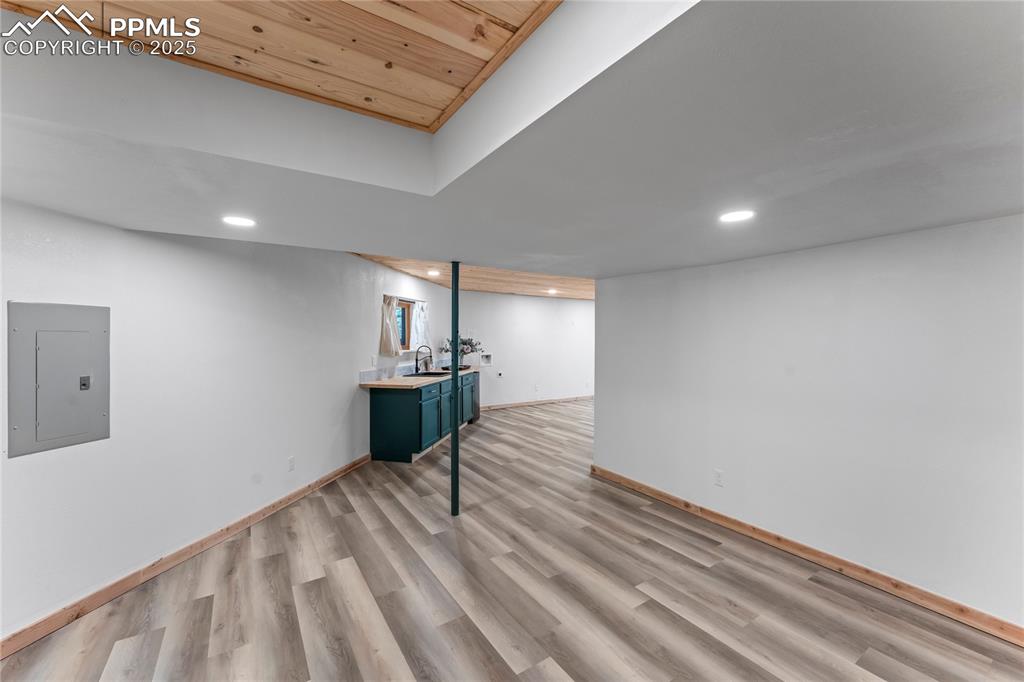 Image 28 of 49: Finished basement featuring electric panel, light wood-type flooring, wood