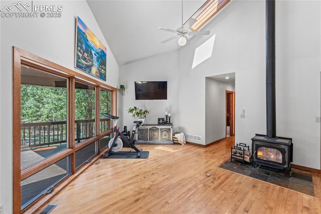 Image 4 of 49: Exercise room with a wood stove, wood finished floors, high vaulted ceiling