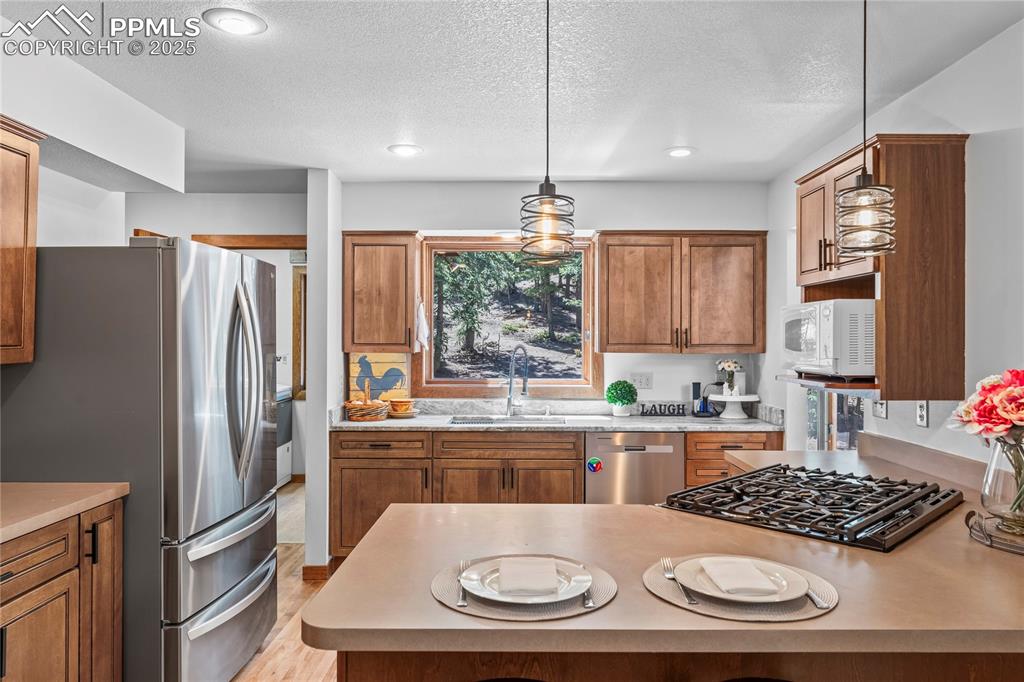 Image 7 of 49: Kitchen with appliances with stainless steel finishes, brown cabinets, a te