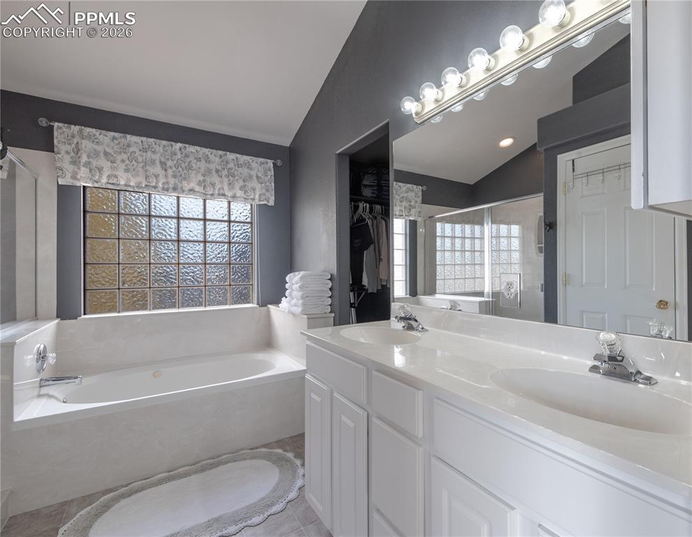 Image 12 of 50: Full primary bath en suite with vaulted ceiling, a stall shower, a bath, do