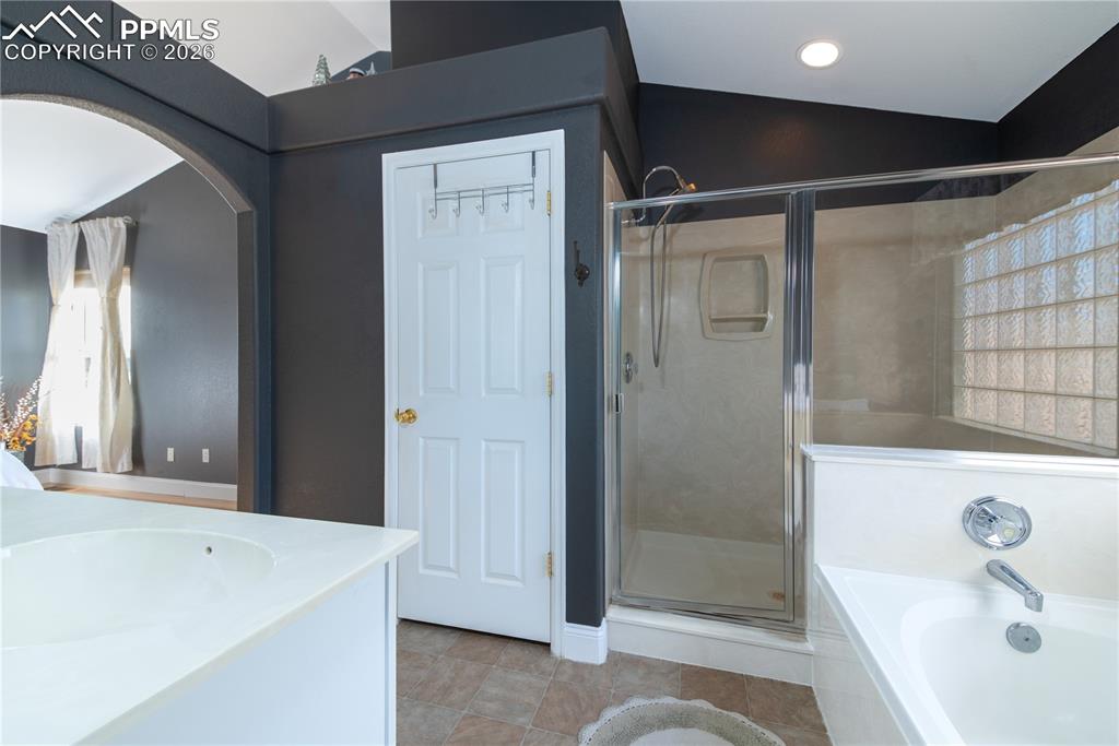 Image 13 of 50: Full primary bath en suite with vaulted ceiling, a stall shower, a bath, do