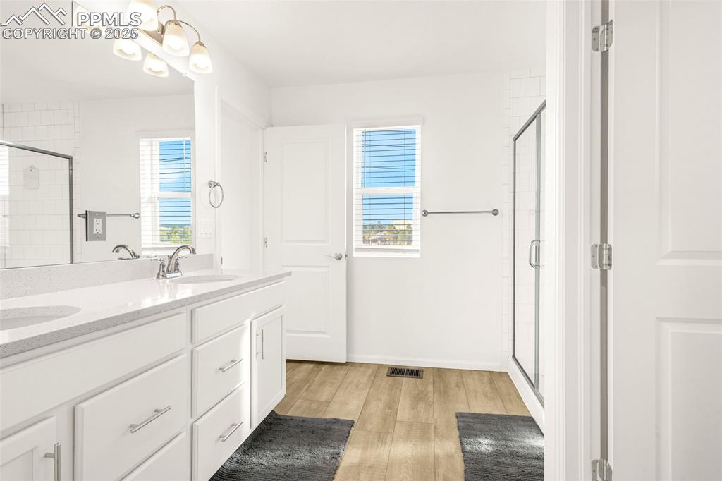 Image 12 of 38: Bathroom featuring a shower stall, wood finished floors, and double vanity