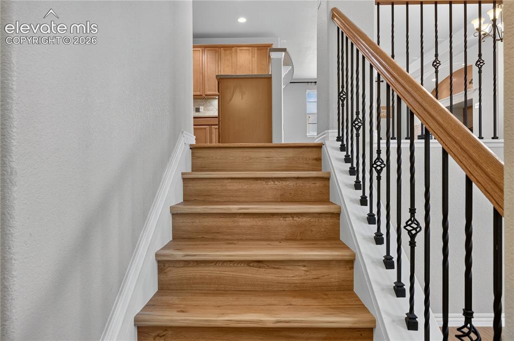 Image 13 of 43: Staircase featuring brand new LVP treads, a wooden handrail, and wrought-ir
