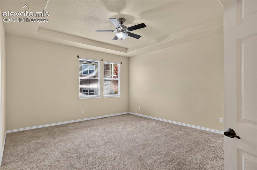 Image 26 of 43: Primary bedroom featuring a tray ceiling, wall-to-wall carpeting, and a cen