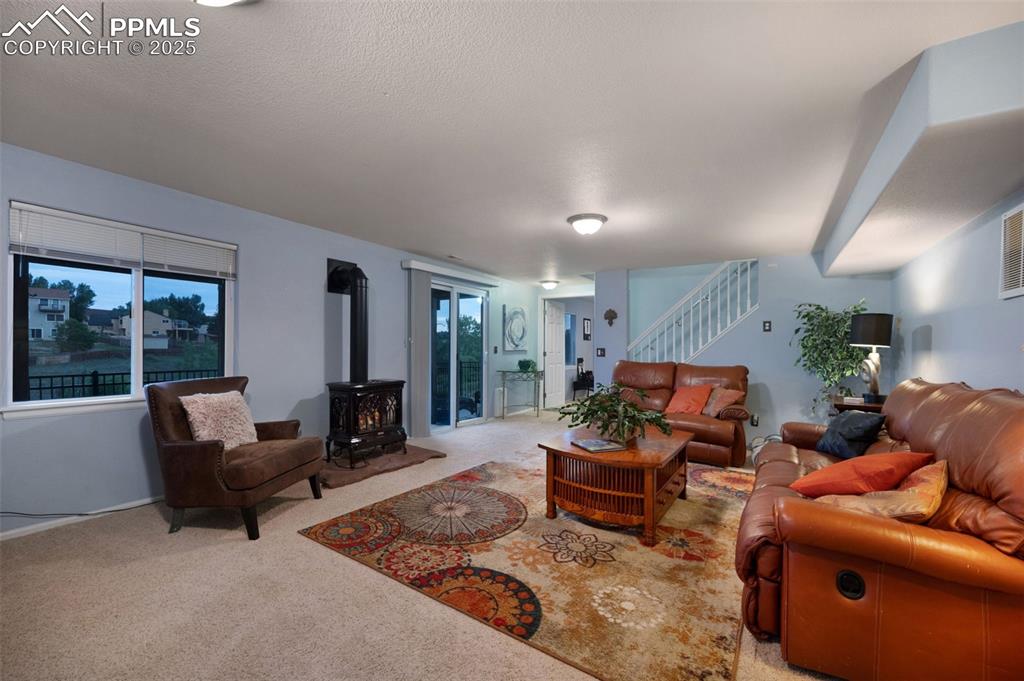 Image 27 of 49: Carpeted living area with a wood stove, stairs, healthy amount of natural l
