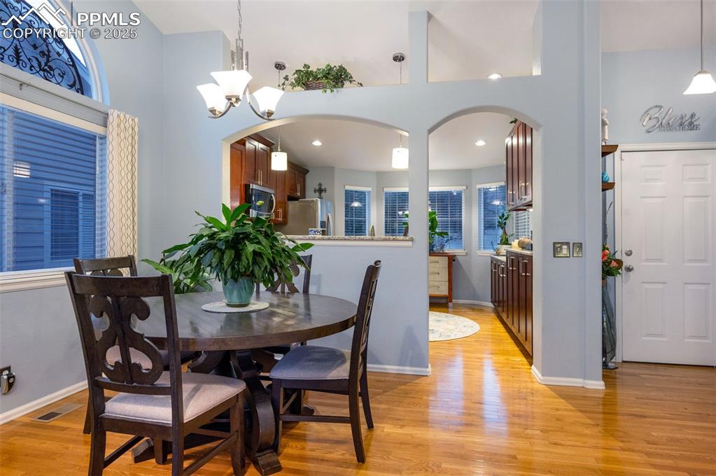 Image 5 of 49: Dining room with arched walkways, light wood finished floors, and a high ce