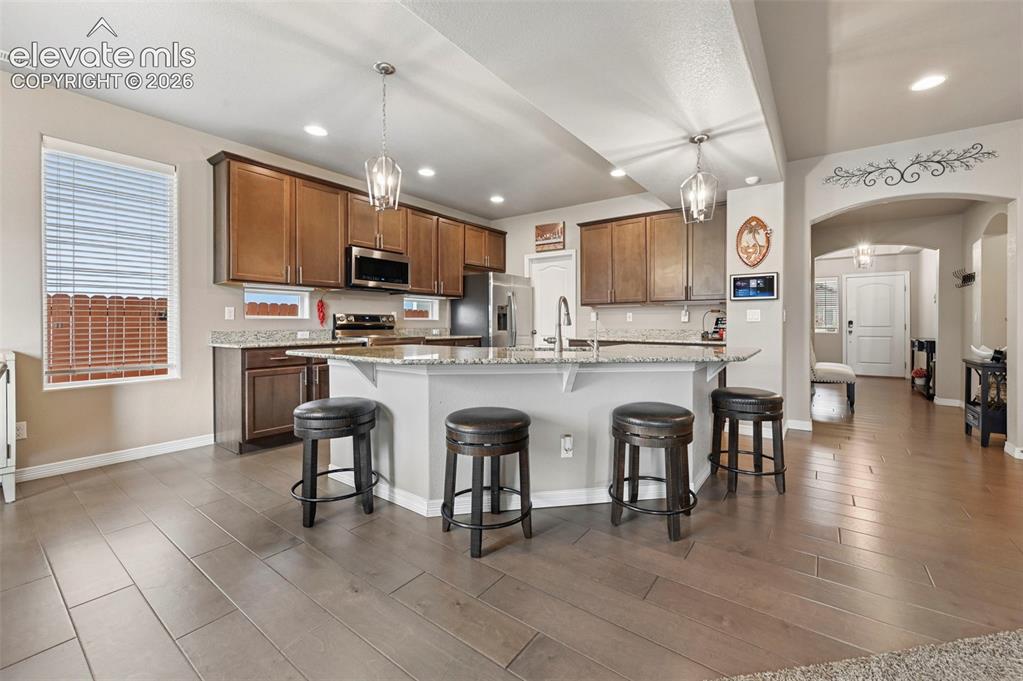 Image 5 of 24: Expansive kitchen with wood-finish flooring, a large island featuring a bui