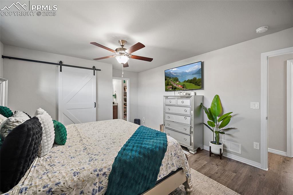 Image 22 of 36: Bedroom with a barn door, dark wood-style flooring, ceiling fan, and a spac