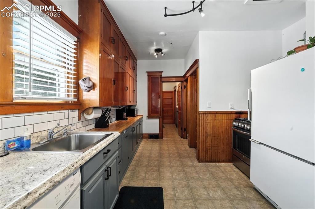 Image 25 of 48: Kitchen with white appliances, light countertops, a wainscoted wall, wooden