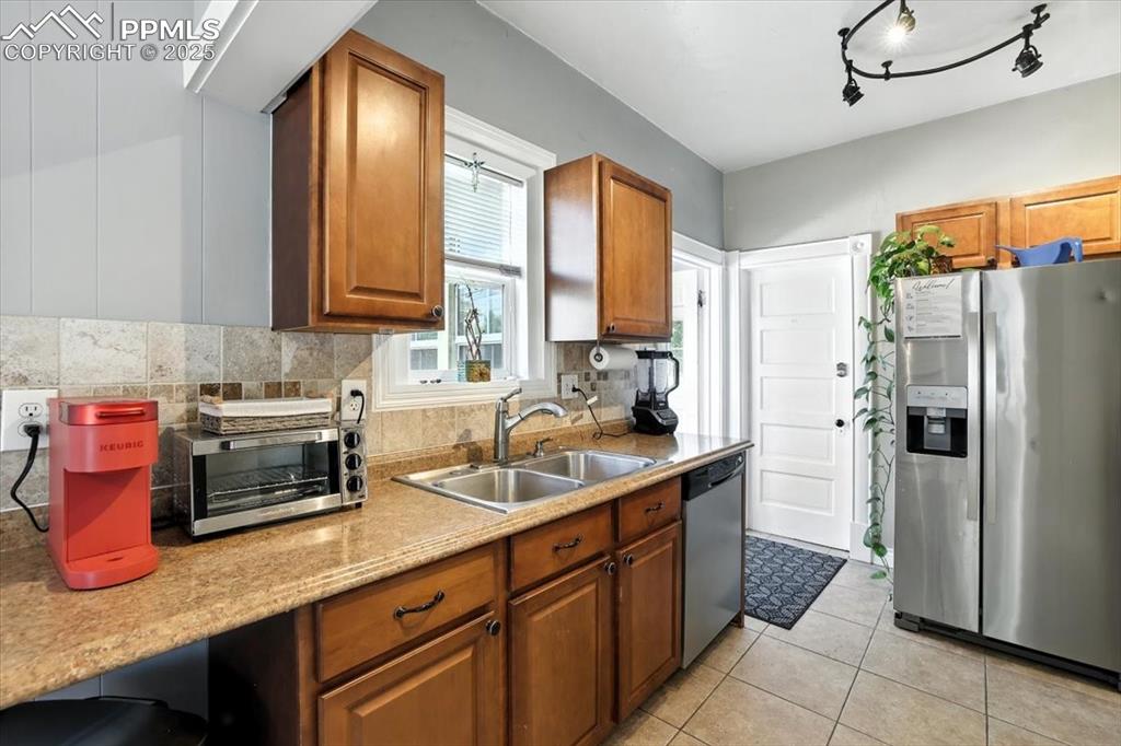 Image 5 of 48: Kitchen with stainless steel appliances, brown cabinetry, light tile patter