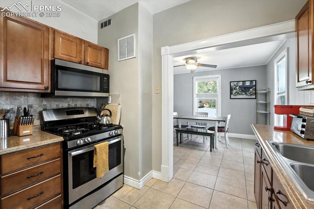 Image 6 of 48: Kitchen with stainless steel appliances, brown cabinets, and light tile pat