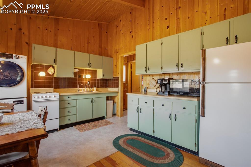 Image 11 of 38: Kitchen with wood ceiling, stacked washer and dryer, wooden walls, and whit