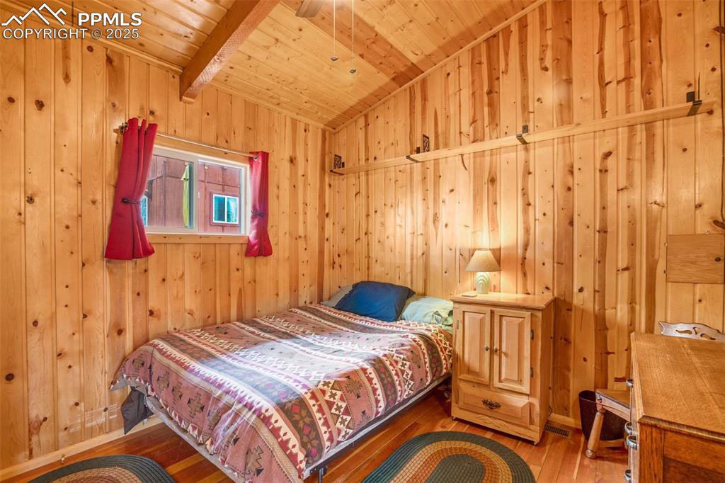 Image 14 of 38: Bedroom with wooden ceiling, wood walls, wood-type flooring, and vaulted ce