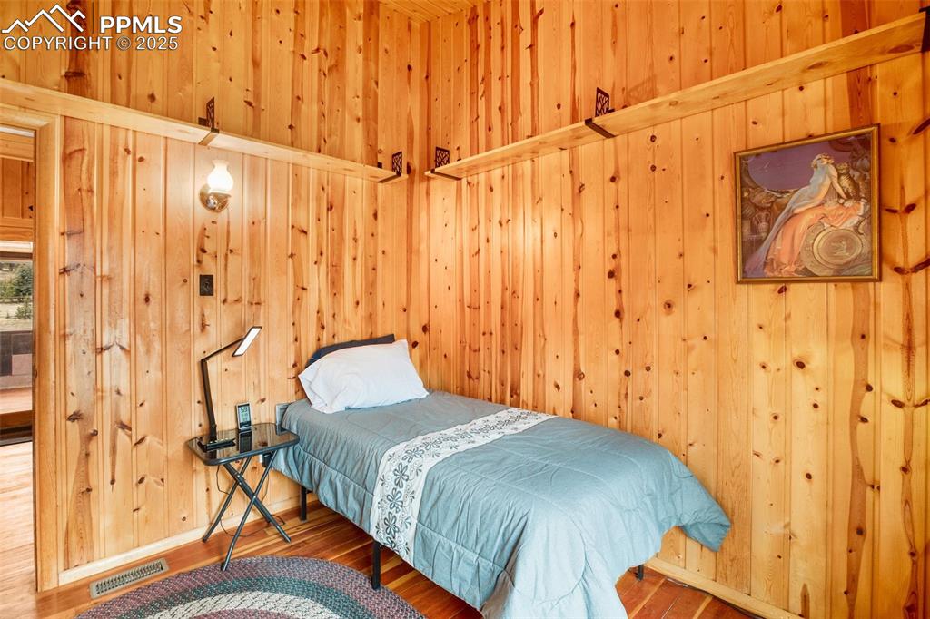 Image 15 of 38: Bedroom with wood finished floors, wood walls, and visible vents